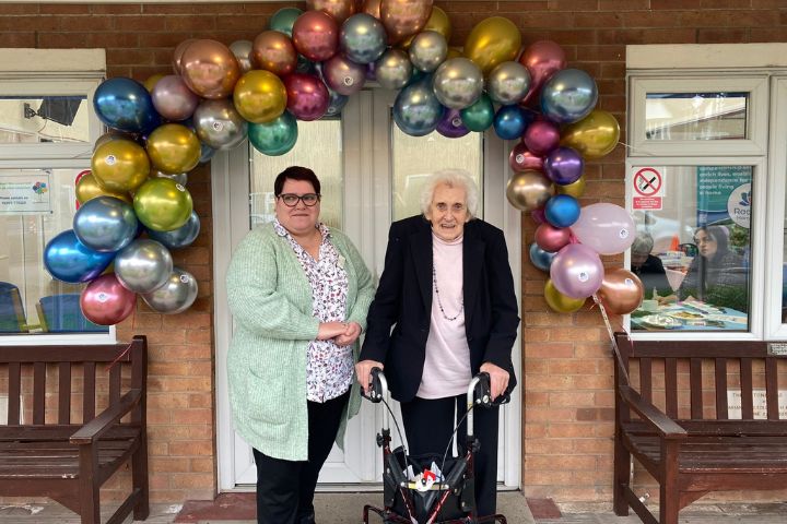 client and carer stood underneath a balloon arch