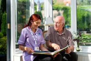 A Radfield Home Care professional and an older adult share a moment of connection while looking through a photo album, showcasing companionship care in Bexhill.