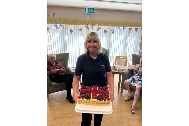 Julie from Radfield Home Care Chester smiling while holding a freshly baked cake during VE Day celebrations.