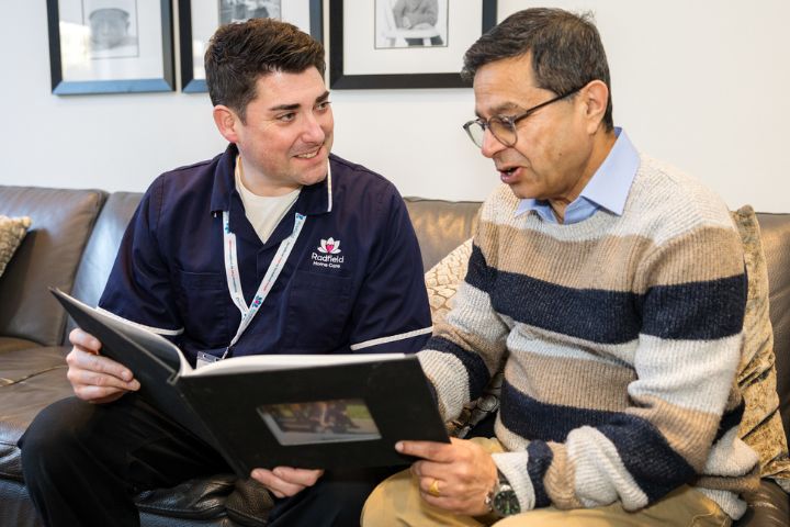 Care professional and older client sharing memories over a photo album in a cosy living room; highlighting Radfield Home Care’s award-winning, person-centred approach as a trusted home care provider in the UK