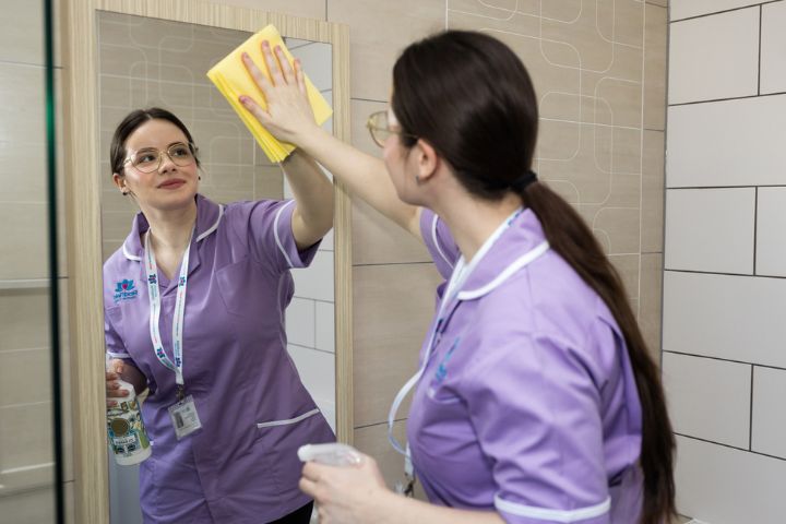 Radfield Home Care professional delivering live in care support while cleaning a mirror in a client’s home – showcasing practical, compassionate care from a top 20 home care group