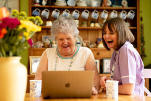care professional sat by a laptop with a client